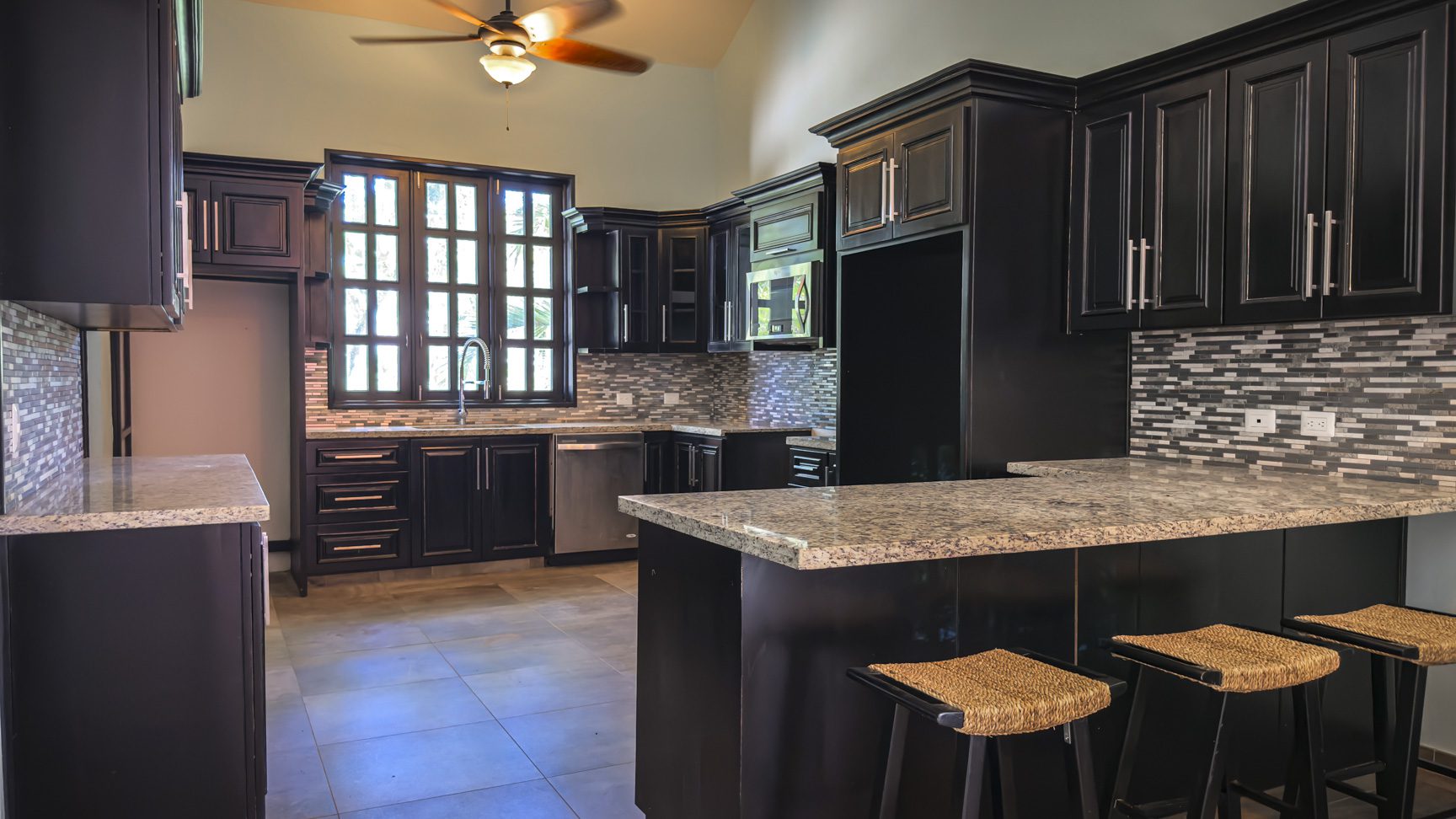 buyDRproperty Modern kitchen design with black cabinets, granite countertops, and bar seating. Sosua Real Estate