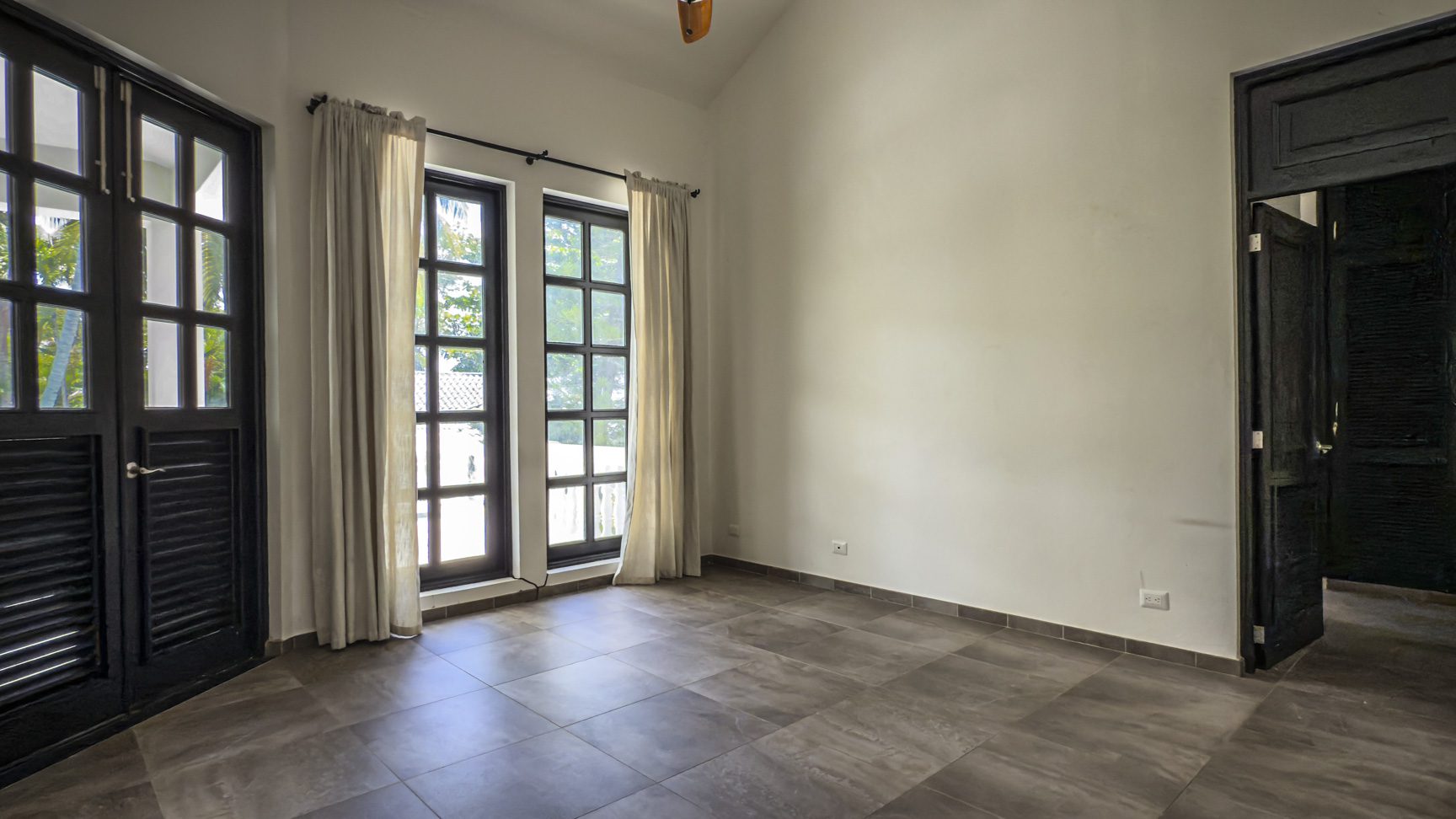 buyDRproperty Empty room with black doors, windows, and neutral curtains, ready for home design. Sosua Real Estate