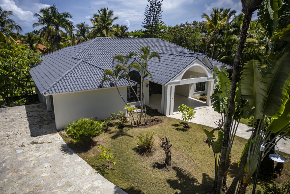 buyDRproperty Modern Caribbean villa with gray tile roof, palm trees, and lush landscaping. Sosua Real Estate