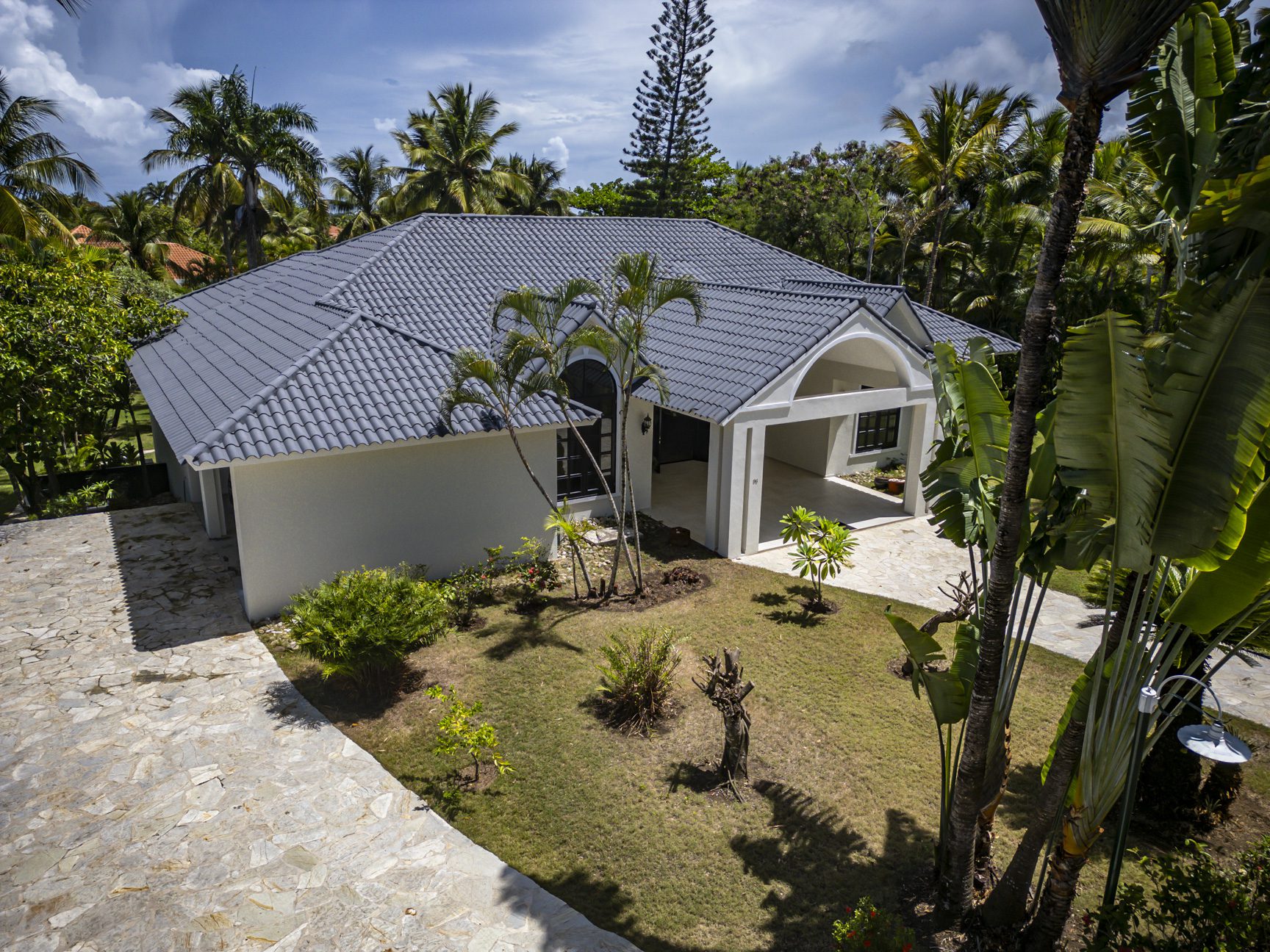 buyDRproperty Modern Caribbean villa with gray tile roof, palm trees, and lush landscaping. Sosua Real Estate