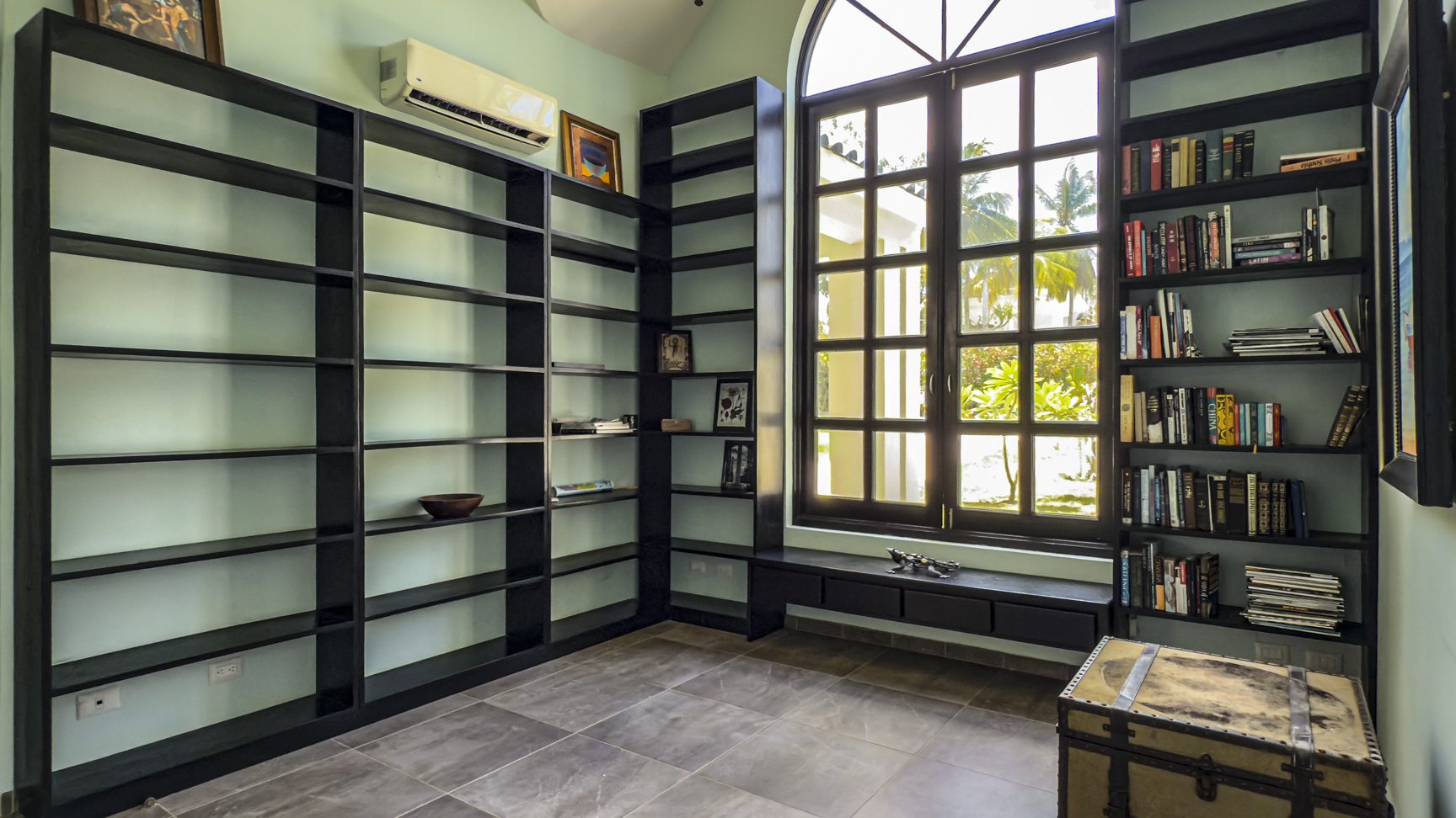 buyDRproperty Home library with black bookshelves, a large window, and a vintage trunk. Sosua Real Estate