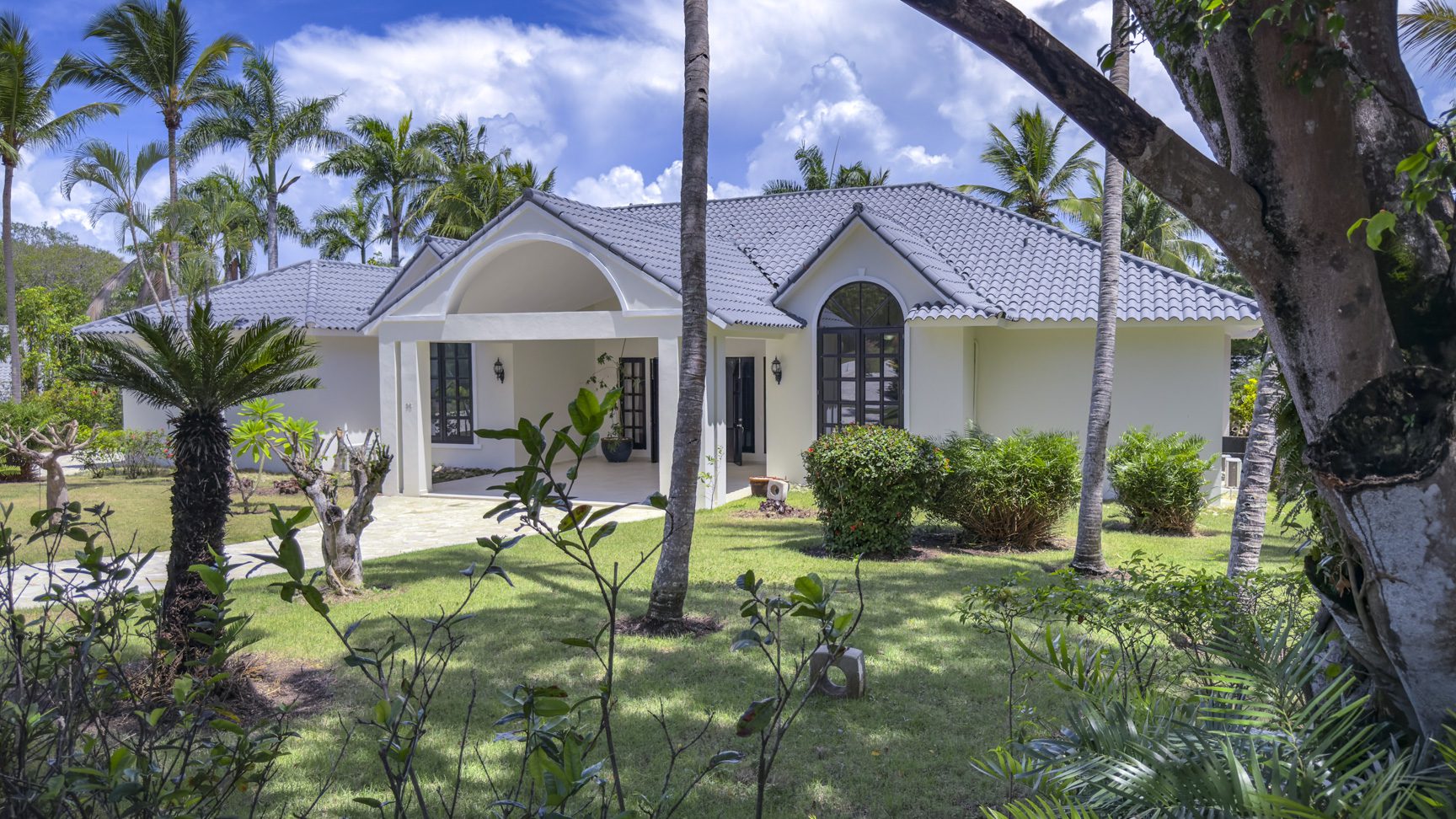 buyDRproperty Luxury tropical villa with gray tile roof and lush landscaping, perfect for Caribbean vacation rentals. Sosua Real Estate