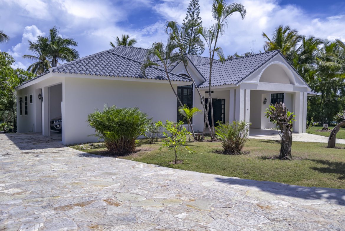 buyDRproperty White tropical home with gray tile roof and stone driveway, surrounded by palm trees Sosua Real Estate