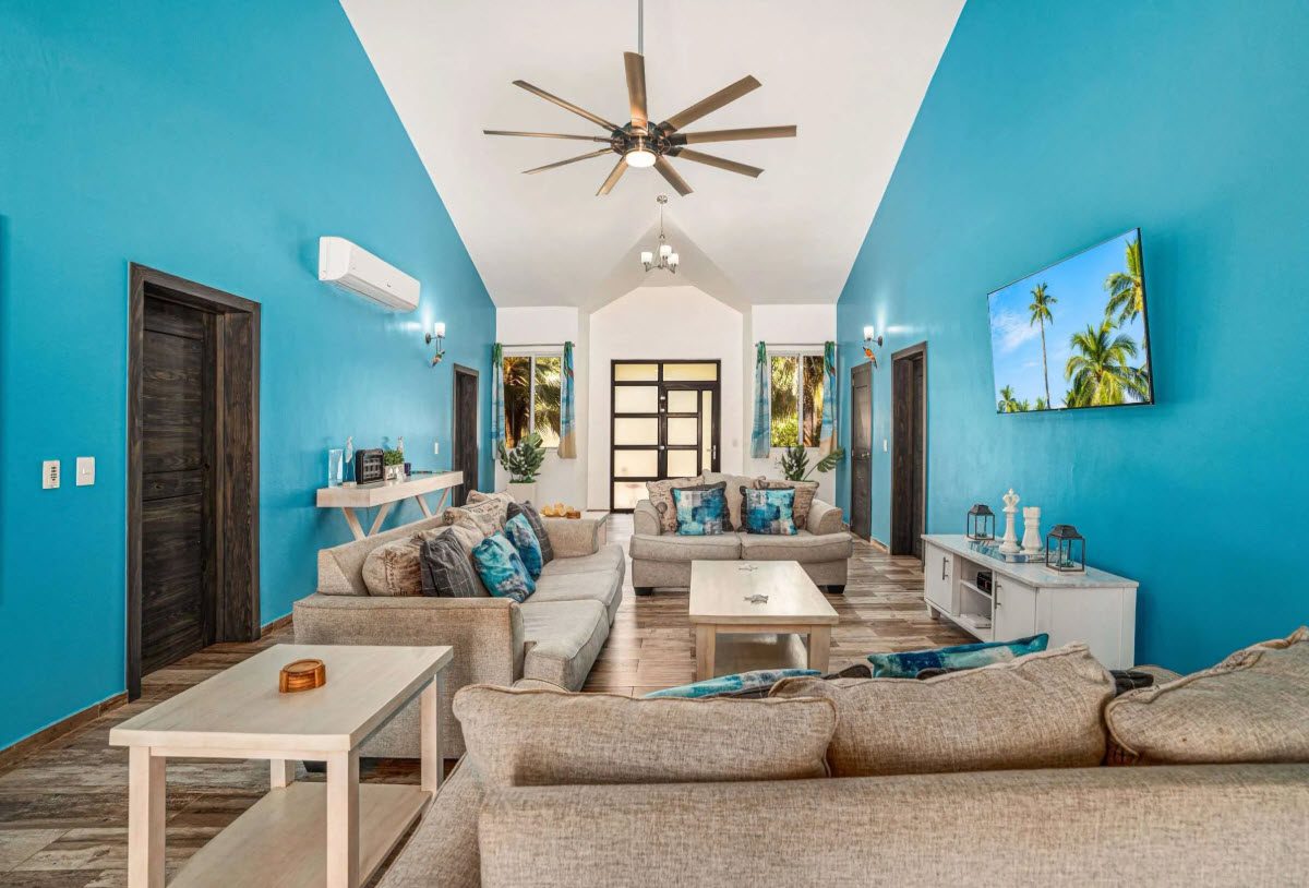 buyDRproperty Elegant living room with blue walls, couches, and a TV showing palm trees. Sosua Real Estate