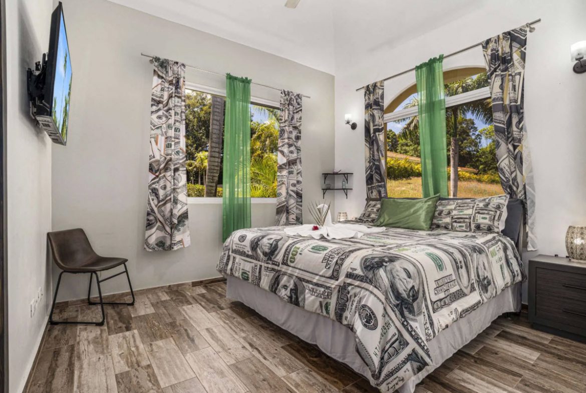 buyDRproperty Elegant bedroom in Villa Lotus with dollar bill-themed bedding and green curtains. Sosua Real Estate