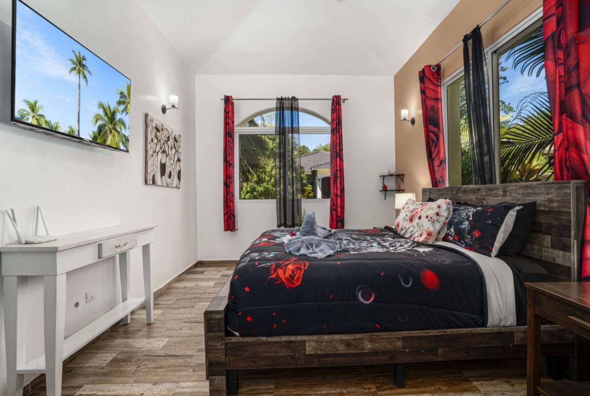buyDRproperty Elegant bedroom in Villa Lotus with a dark floral comforter and palm tree view. Sosua Real Estate