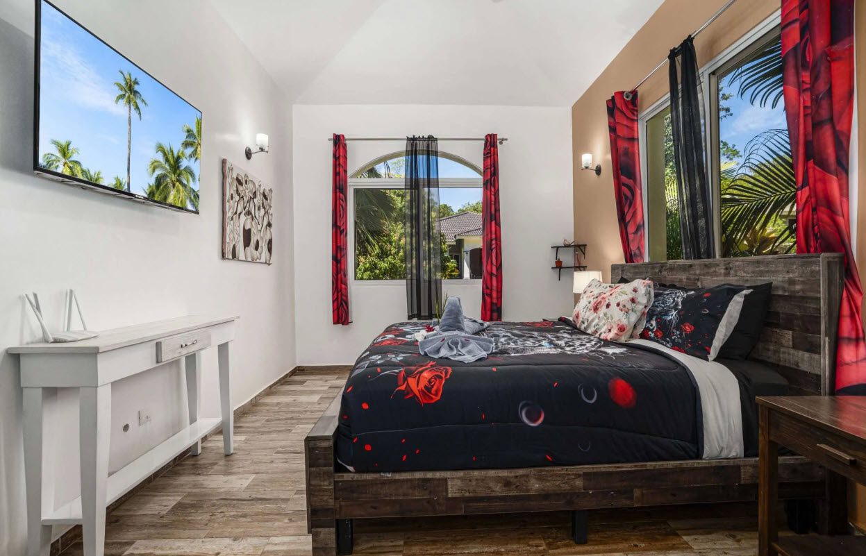 buyDRproperty Elegant bedroom in Villa Lotus with a dark floral comforter and palm tree view. Sosua Real Estate