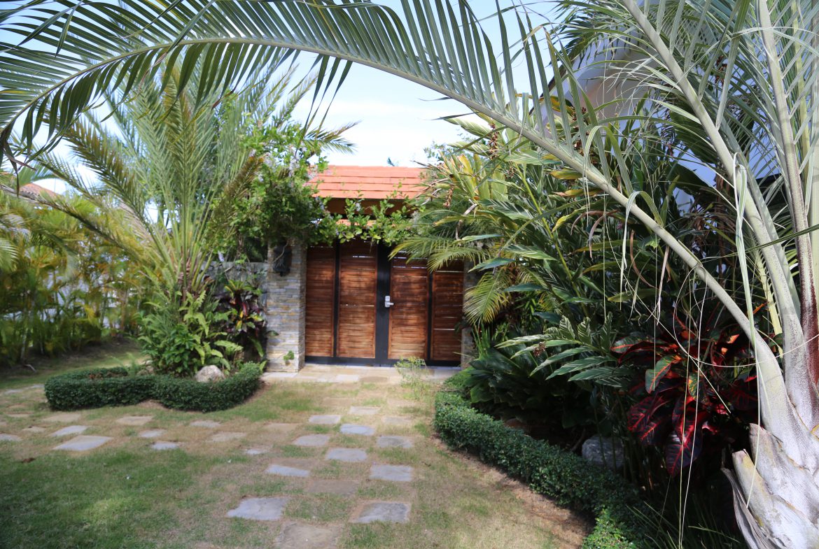 buyDRproperty Tropical garden pathway leading to a wooden door surrounded by lush greenery Sosua Real Estate