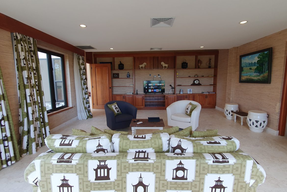 buyDRproperty Luxury living room with patterned sofa, armchairs, built-in entertainment center, and landscape painting. Sosua Real Estate