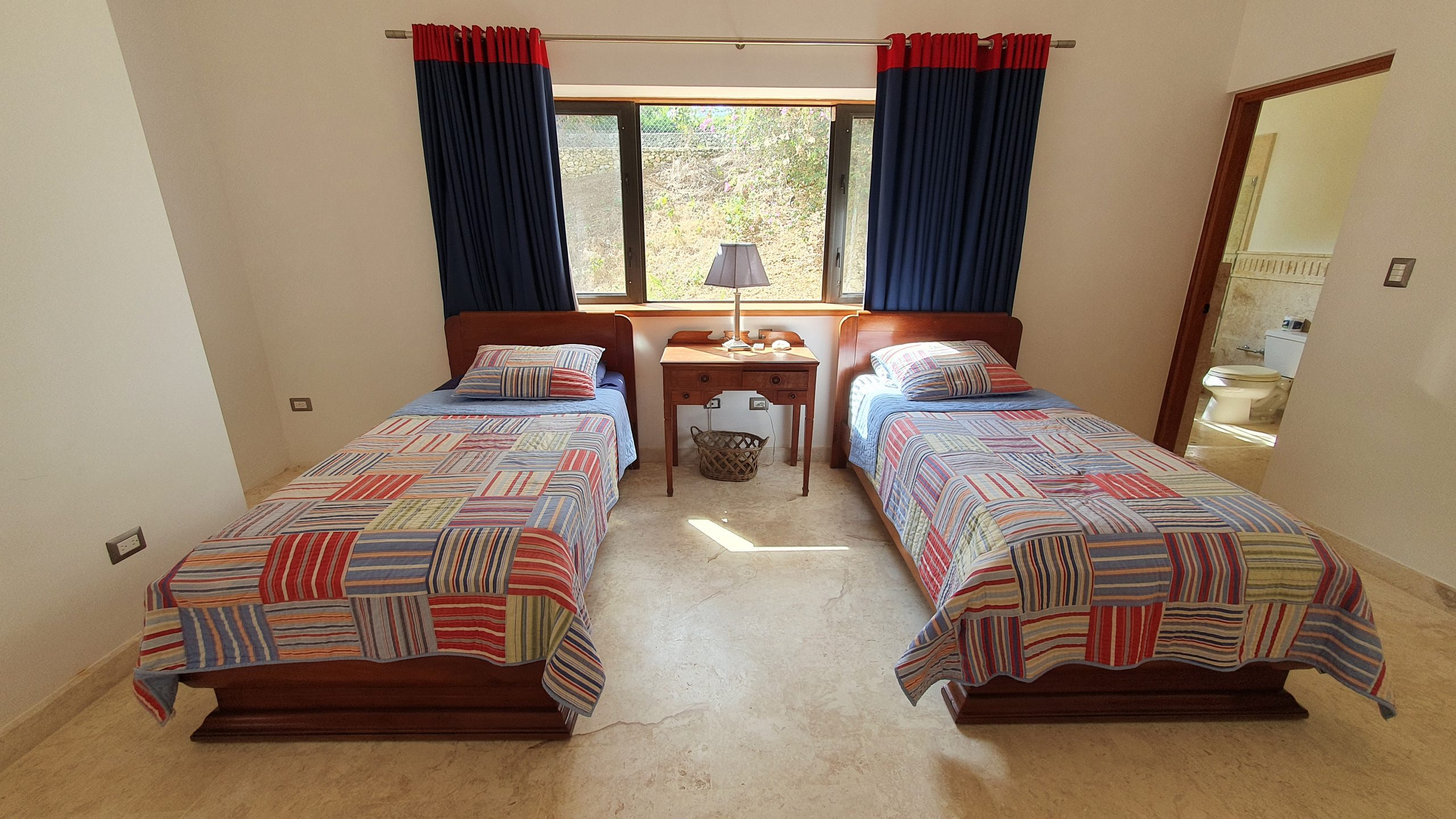 buyDRproperty Cozy guest bedroom with twin beds, patchwork quilts, and blue curtains. Sosua Real Estate