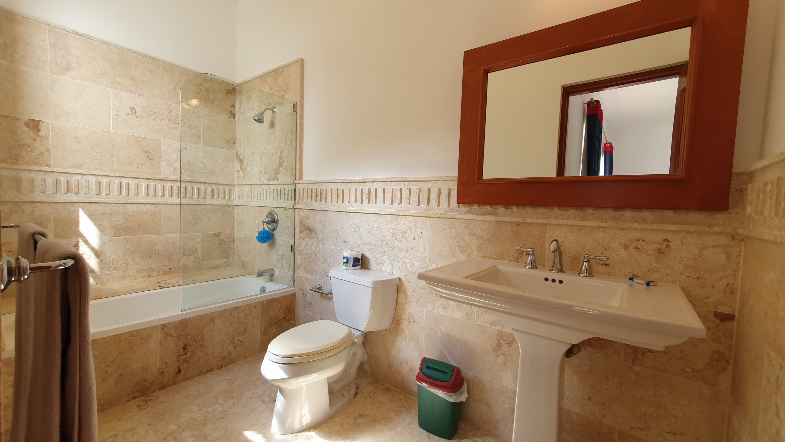 buyDRproperty Travertine tile bathroom with bathtub, pedestal sink, and mirror. Bathroom remodel. Sosua Real Estate