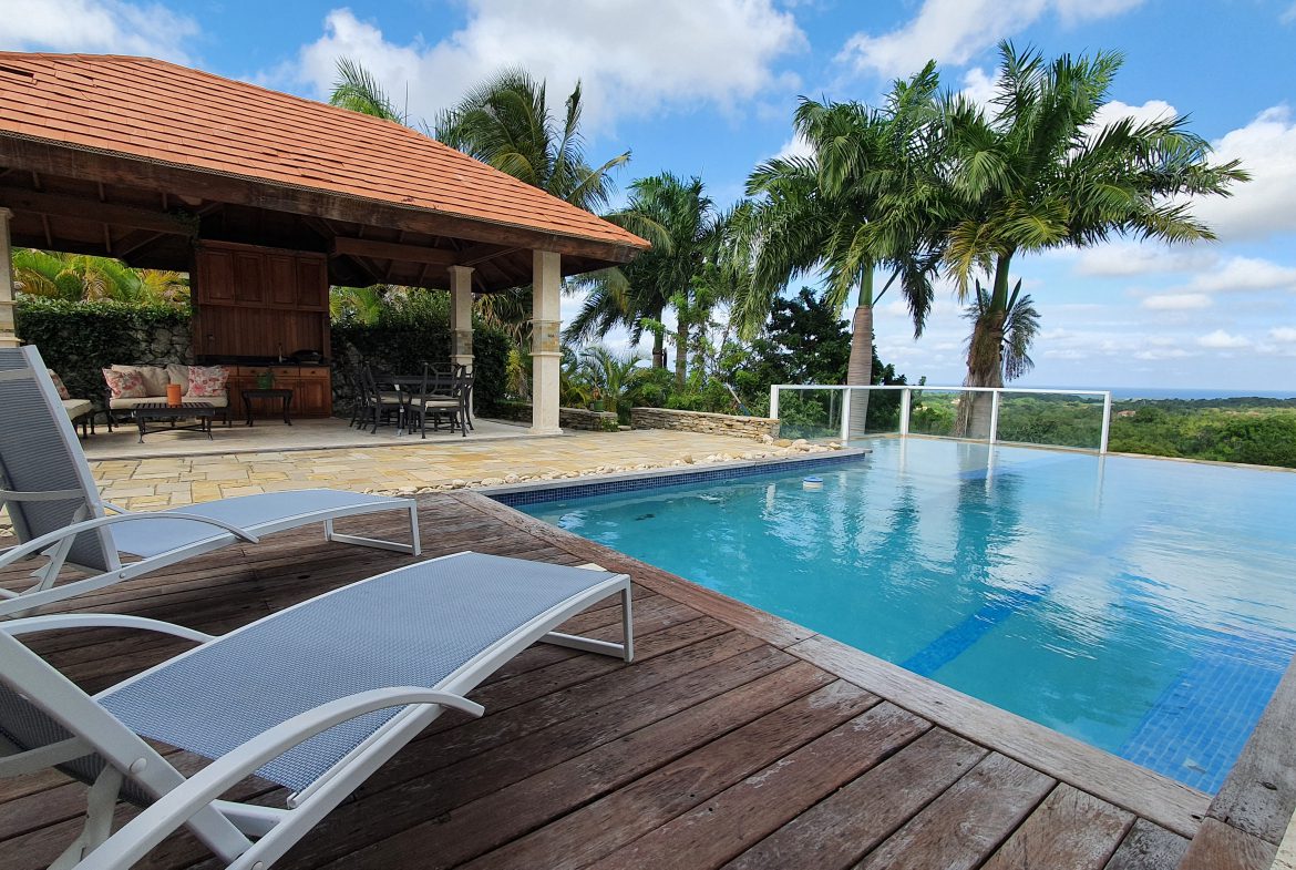 buyDRproperty Luxury villa with infinity pool, lounge chairs, and covered patio overlooking a tropical landscape. Sosua Real Estate