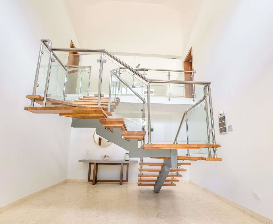 buyDRproperty Modern staircase with wood treads, glass railings, and stainless steel supports in a bright, white entryway. Sosua Real Estate