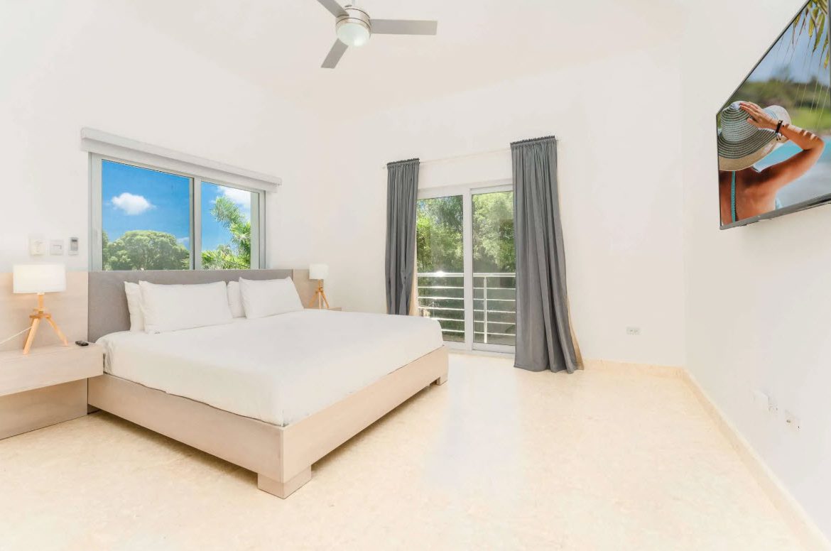buyDRproperty Bright bedroom with king bed, TV, window view, and balcony access. Sosua Real Estate