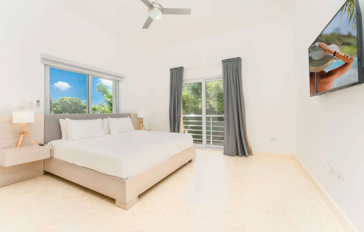 buyDRproperty Bright bedroom with king bed, TV, window view, and balcony access. Sosua Real Estate