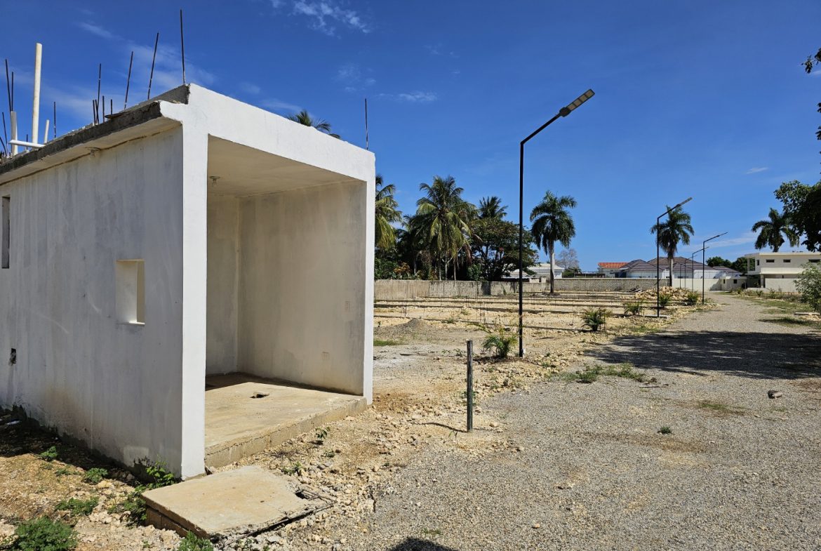 buyDRproperty Unfinished concrete structure on a sunny, empty lot with palm trees in the background. Sosua Real Estate