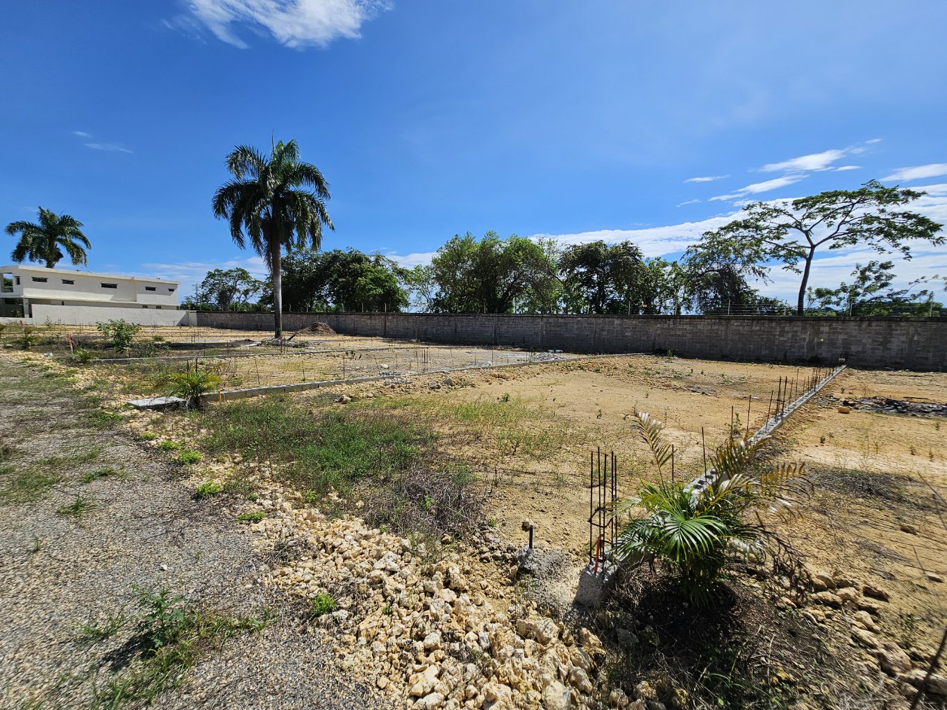 buyDRproperty Construction site with foundation work, palm trees, and blue sky. Sosua Real Estate