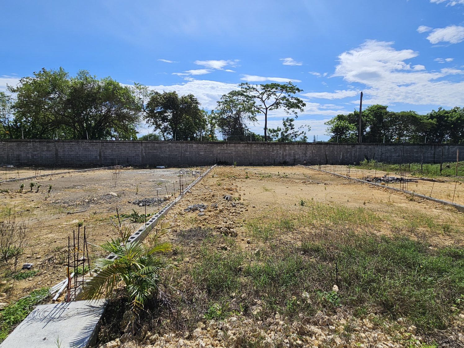 buyDRproperty Cleared land ready for construction, with a block wall in the background under a blue sky. Sosua Real Estate
