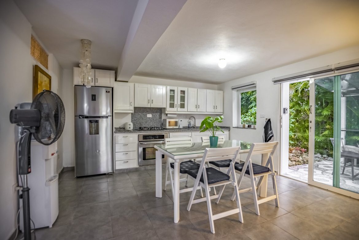 buyDRproperty Bright kitchen with white cabinets, stainless steel appliances, dining table, and a patio view. Sosua Real Estate
