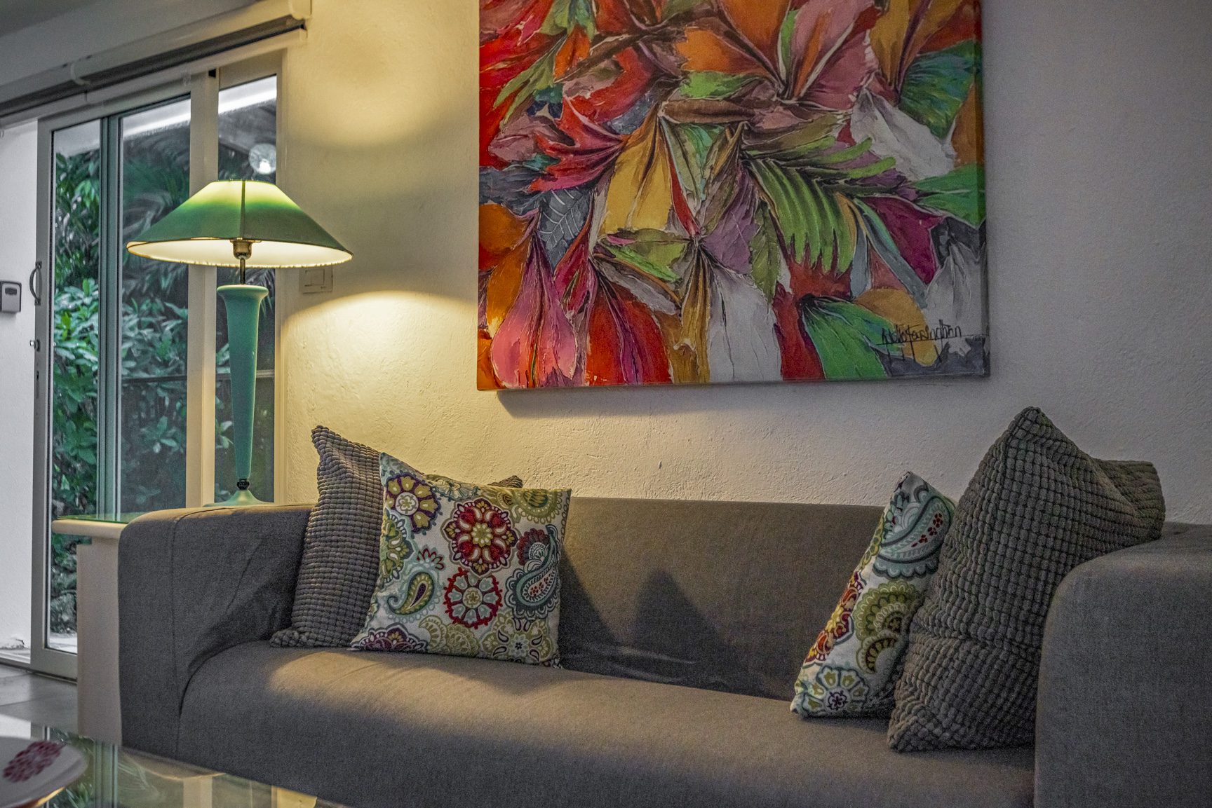 buyDRproperty Living room with gray sofa, colorful floral pillows, green lamp, and vibrant abstract art on the wall. Sosua Real Estate
