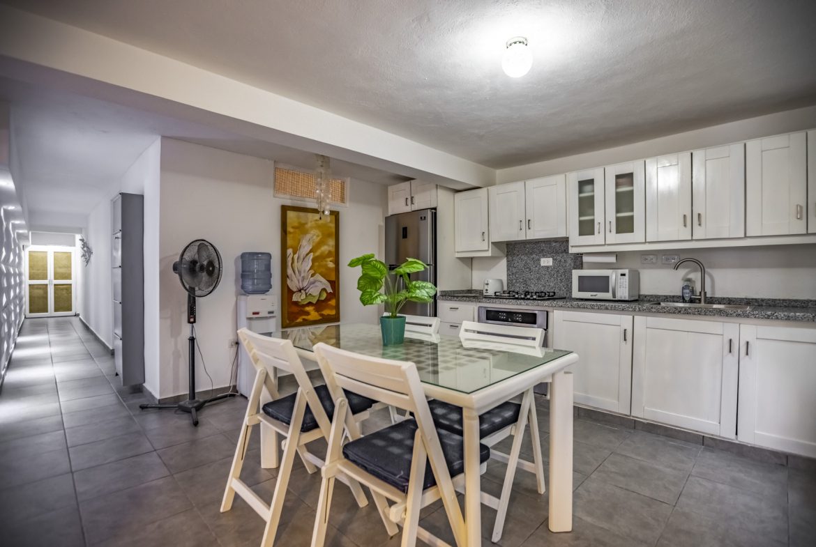 buyDRproperty Bright kitchen with white cabinets, a glass-top table, and a painting. Stainless steel appliances add a modern touch. Sosua Real Estate