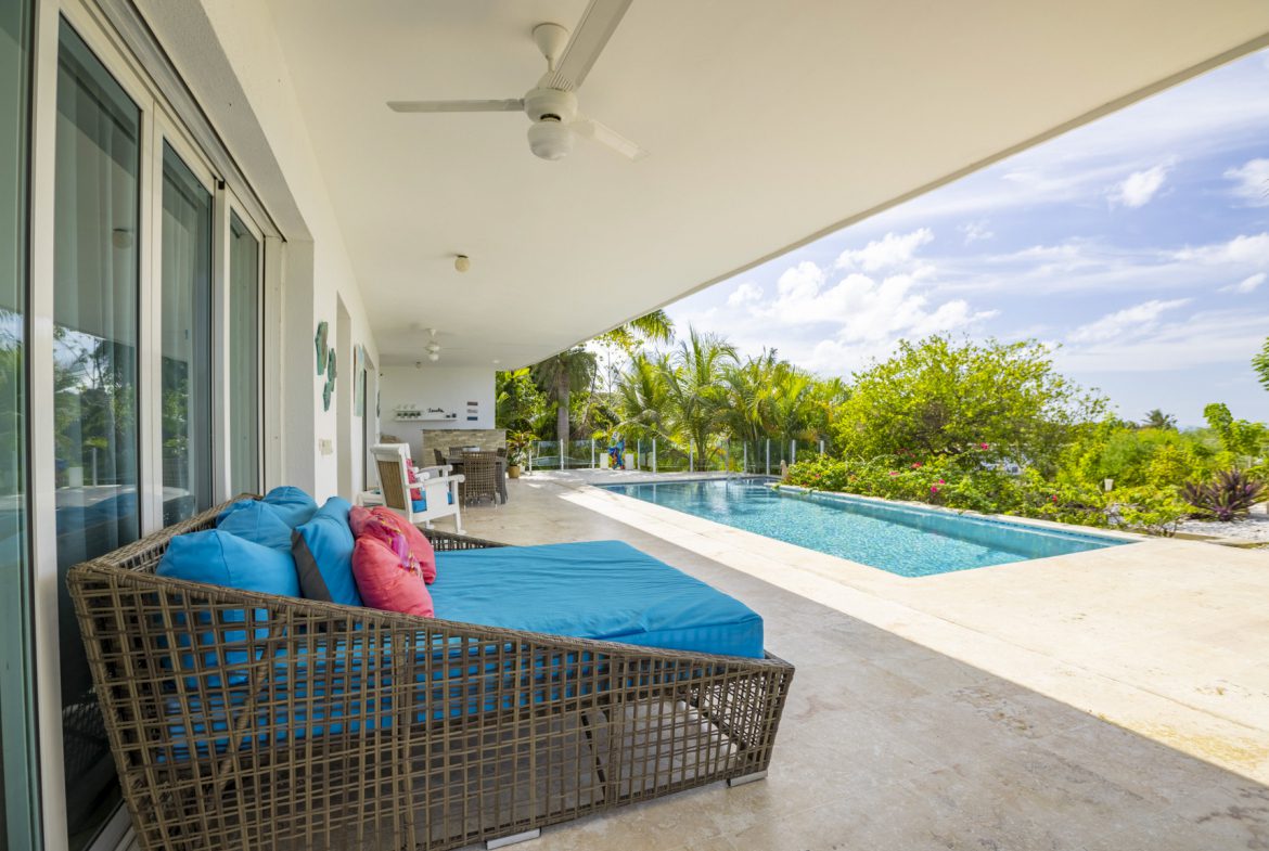 buyDRproperty Luxury pool deck with daybed, turquoise cushions, and tropical landscaping. Sosua Real Estate