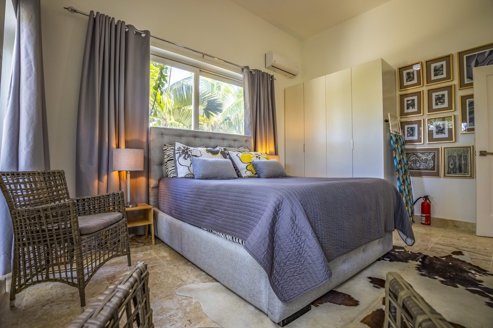 buyDRproperty Bright bedroom with gray bedding, wicker chairs, and framed art on the wall. Sosua Real Estate