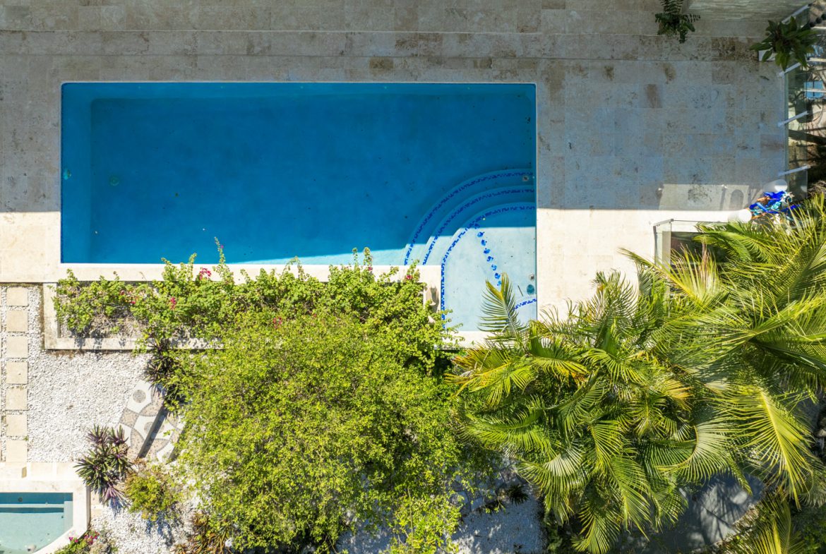 buyDRproperty Aerial view of a turquoise swimming pool surrounded by stone patio, lush greenery, and palm trees. Sosua Real Estate