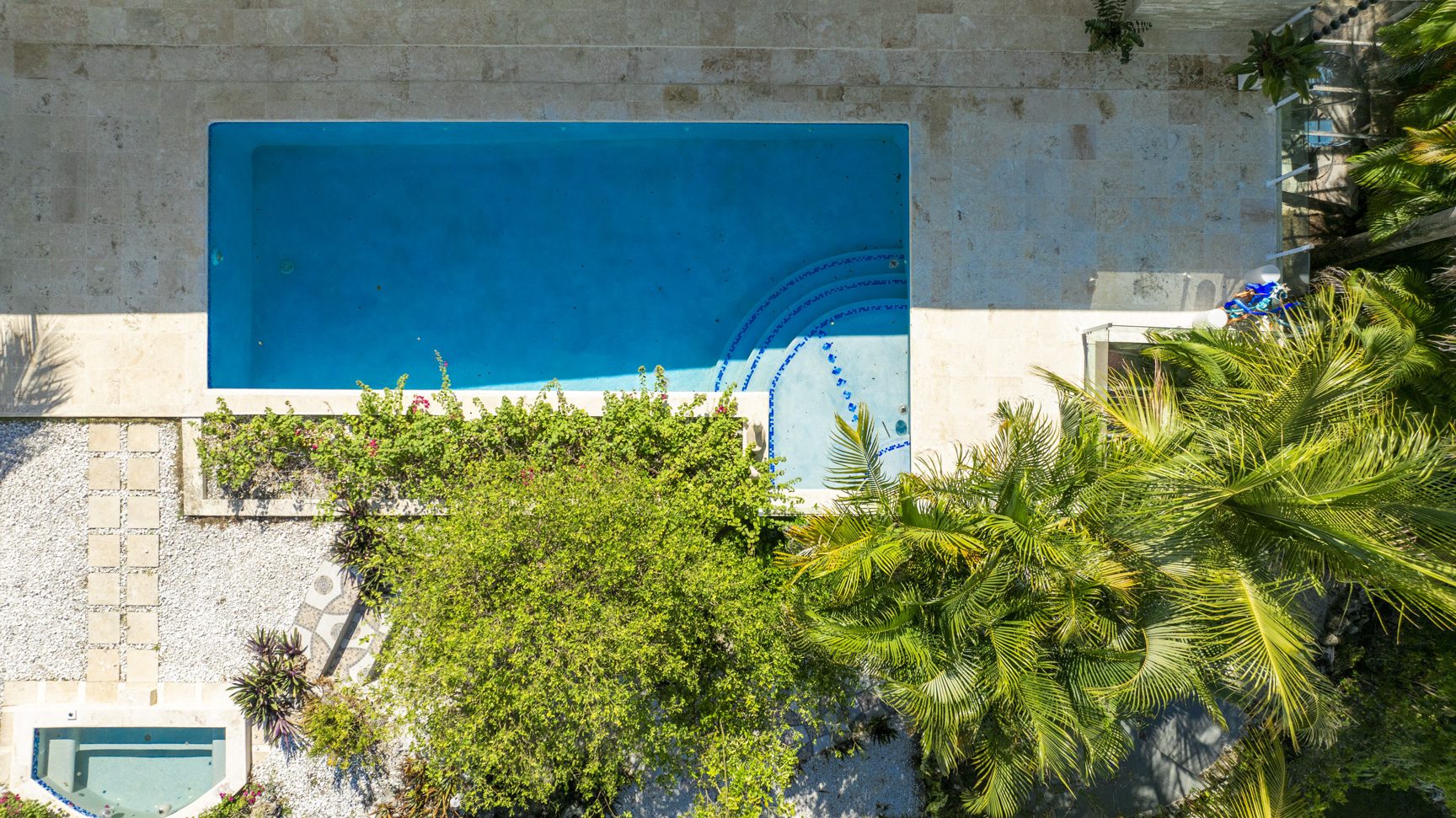 buyDRproperty Aerial view of a turquoise swimming pool surrounded by stone patio, lush greenery, and palm trees. Sosua Real Estate