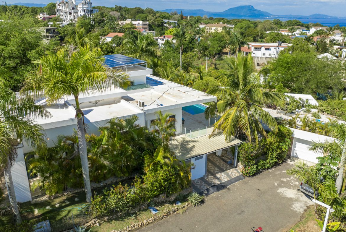 buyDRproperty Aerial view of a modern white villa with solar panels, surrounded by lush tropical greenery. Sosua Real Estate