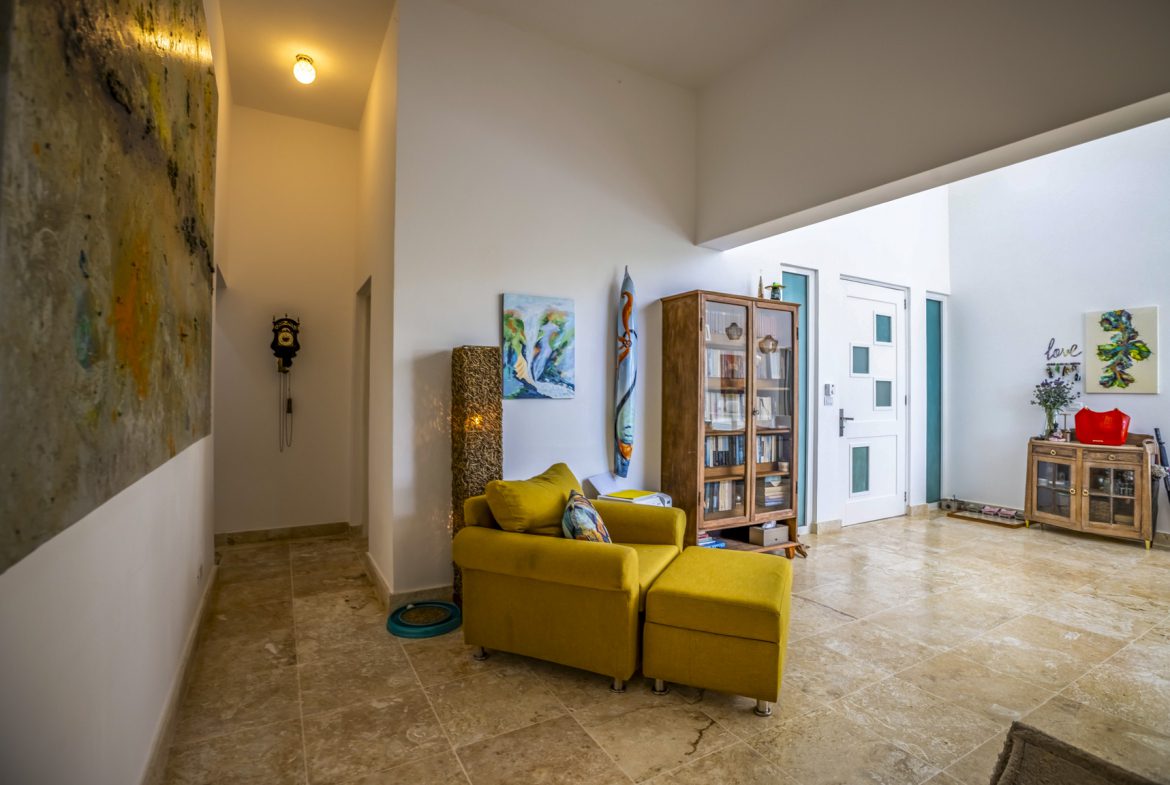 buyDRproperty Sunny living room with yellow armchair, wooden cabinet, and art. Bright interior design. Sosua Real Estate