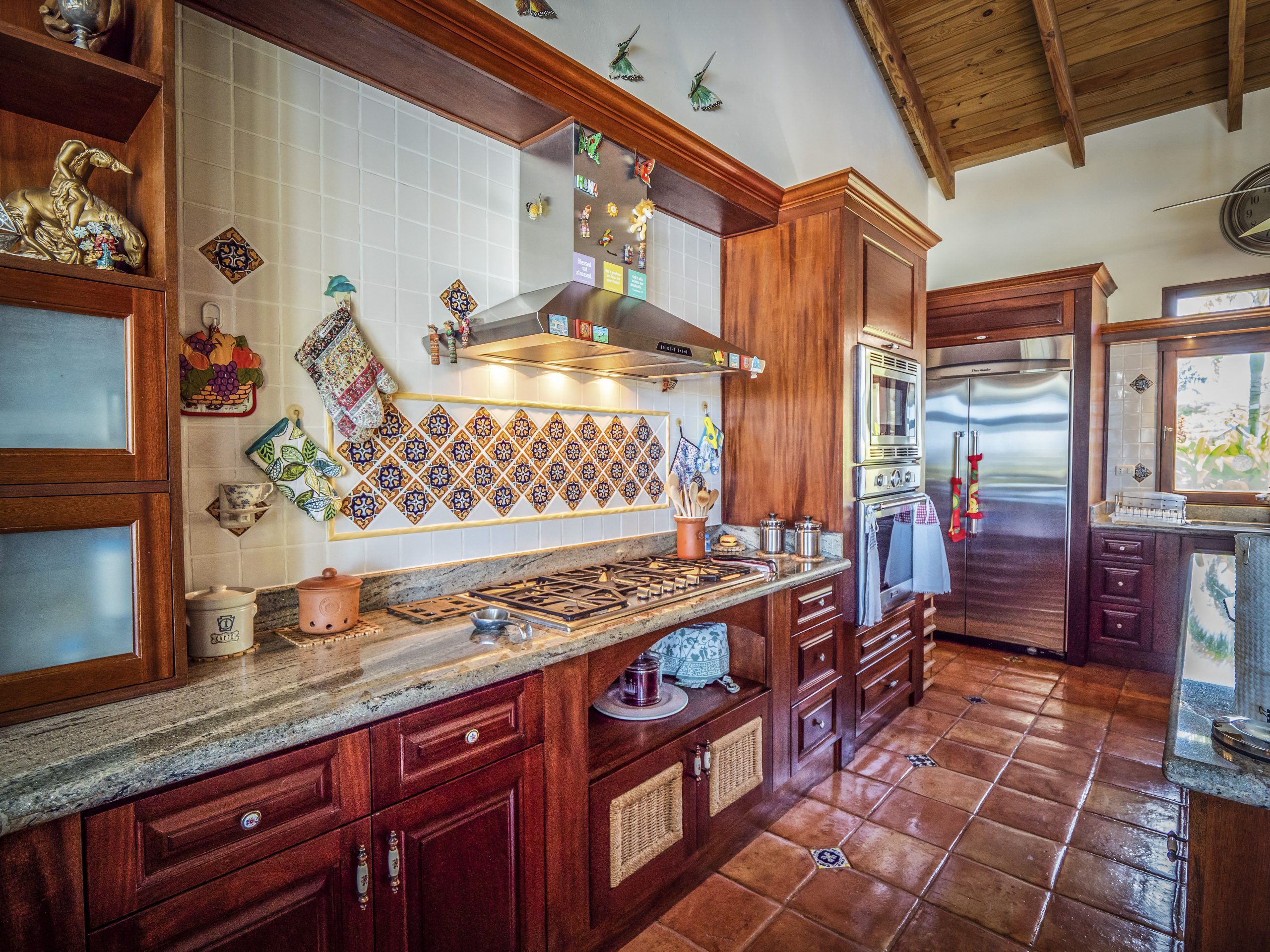 buyDRproperty Rustic kitchen with wooden cabinets, colorful backsplash, and stainless steel appliances Sosua Real Estate