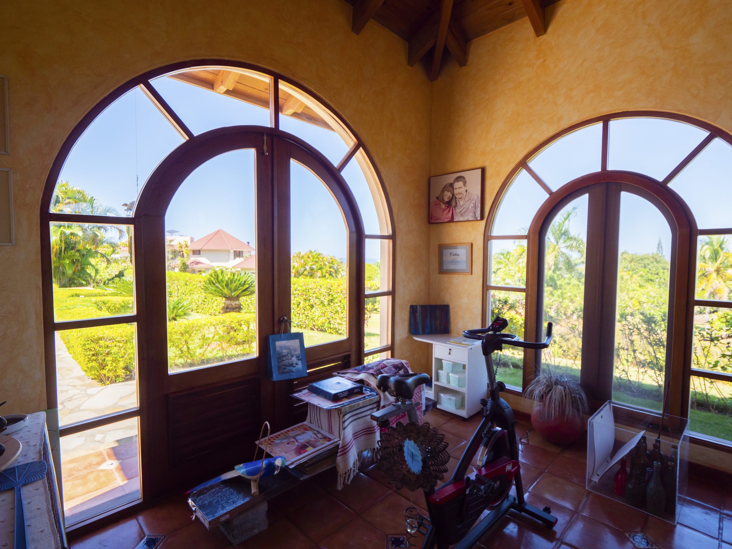 buyDRproperty Bright room with arched windows overlooking a garden and exercise bike inside Sosua Real Estate