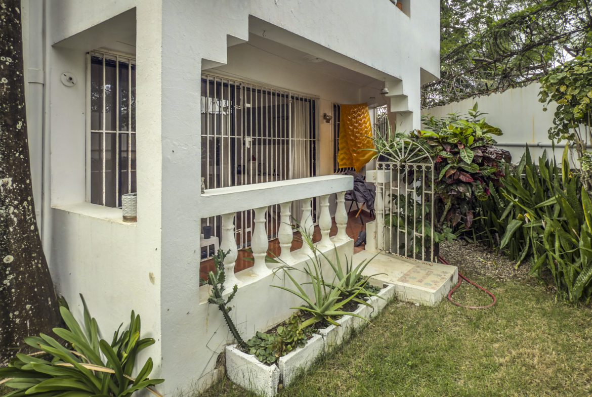 buyDRproperty Exterior view of a 2-bedroom house for sale in Sosúa, featuring a small garden and covered porch. Sosua Real Estate