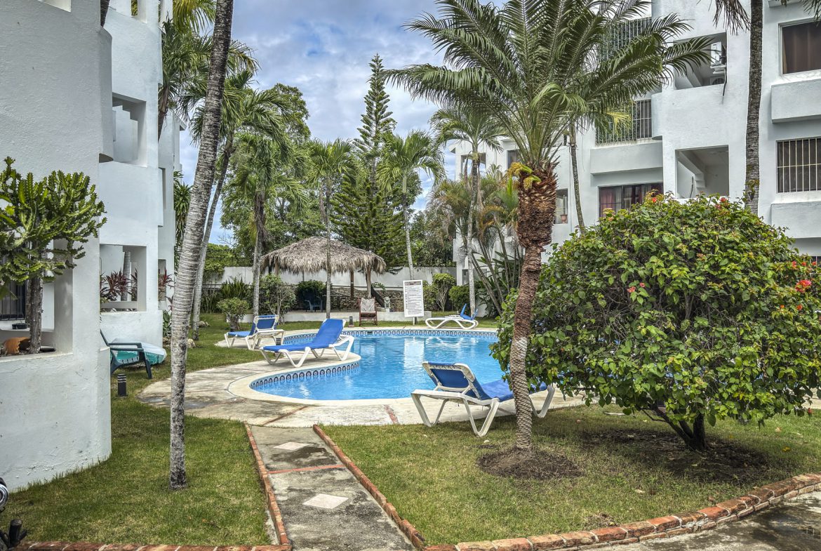 buyDRproperty Sosúa condo complex with a pool, palm trees, and lounge chairs, near playa. Sosua Real Estate