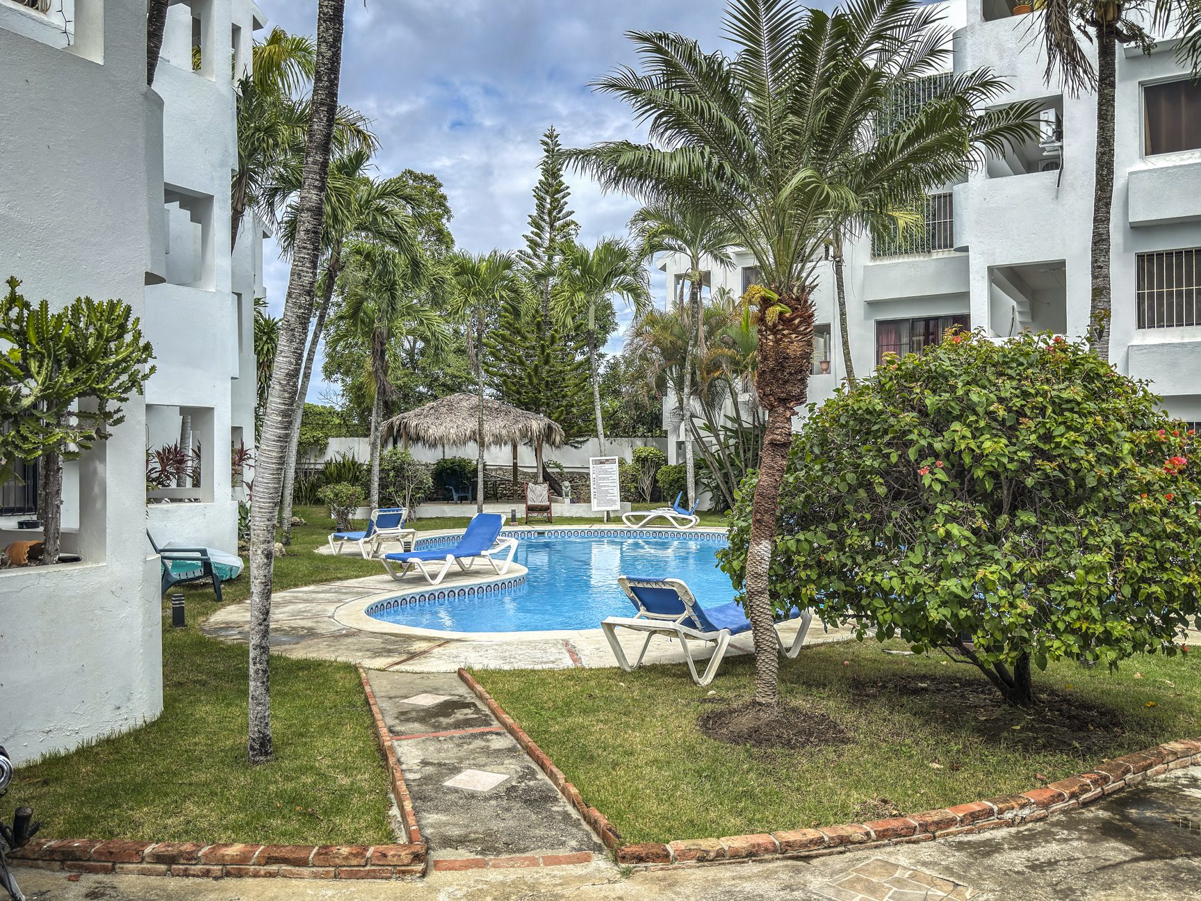 buyDRproperty Sosúa condo complex with a pool, palm trees, and lounge chairs, near playa. Sosua Real Estate