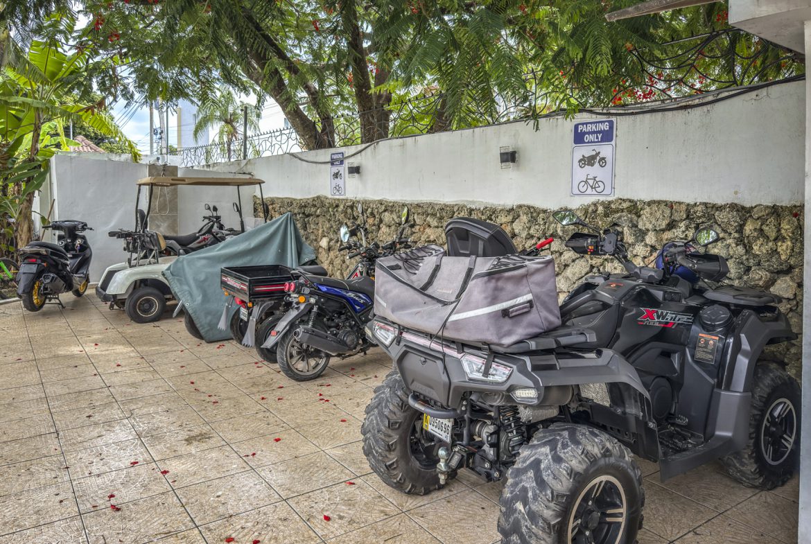 buyDRproperty ATV, motorcycles, and golf cart parked in a designated area with a "Parking Only" sign in Sosúa near playa. Sosua Real Estate