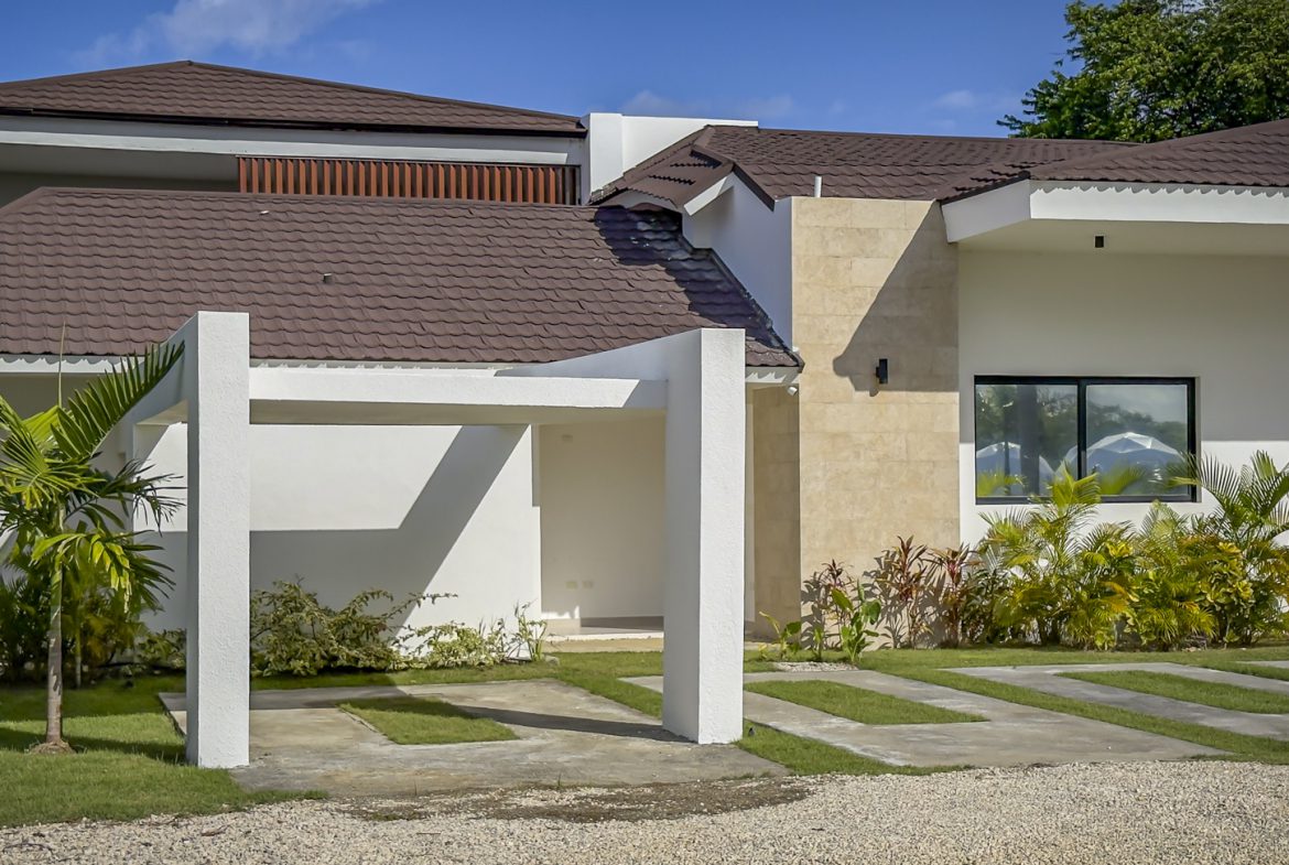 buyDRproperty Exterior of a luxury villa with a modern carport and lush landscaping. Sosua Real Estate