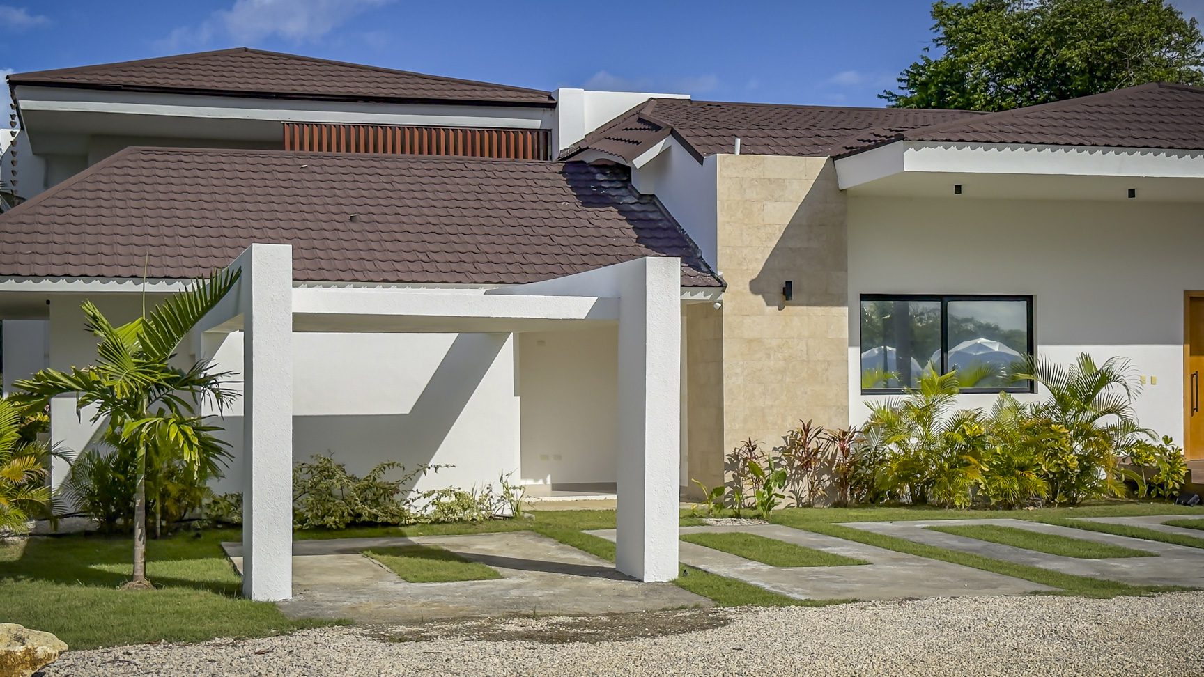 buyDRproperty Exterior of a luxury villa with a modern carport and lush landscaping. Sosua Real Estate