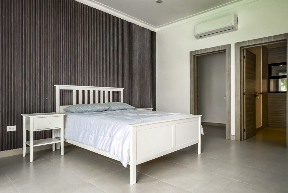 buyDRproperty Luxury villa bedroom with white bed and dark wood accent wall in Sosua Ocean Village. Sosua Real Estate