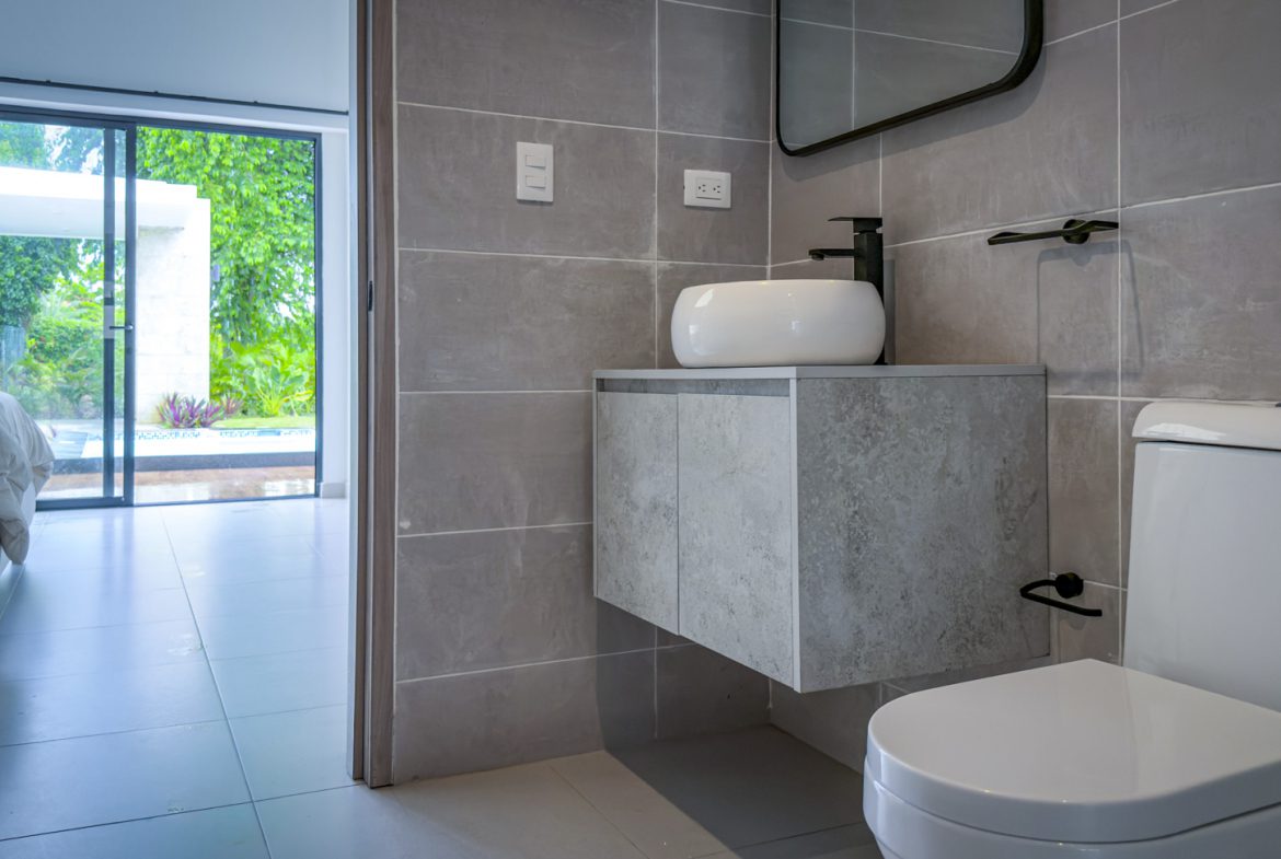 buyDRproperty Modern bathroom with gray tile, white sink, toilet, and view of the luxury villa's pool area. Sosua Real Estate