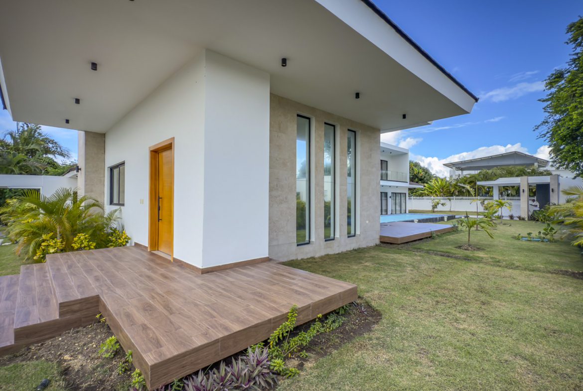 buyDRproperty Luxury villa exterior with wooden deck, modern architecture, and lush green lawn. Sosua Real Estate