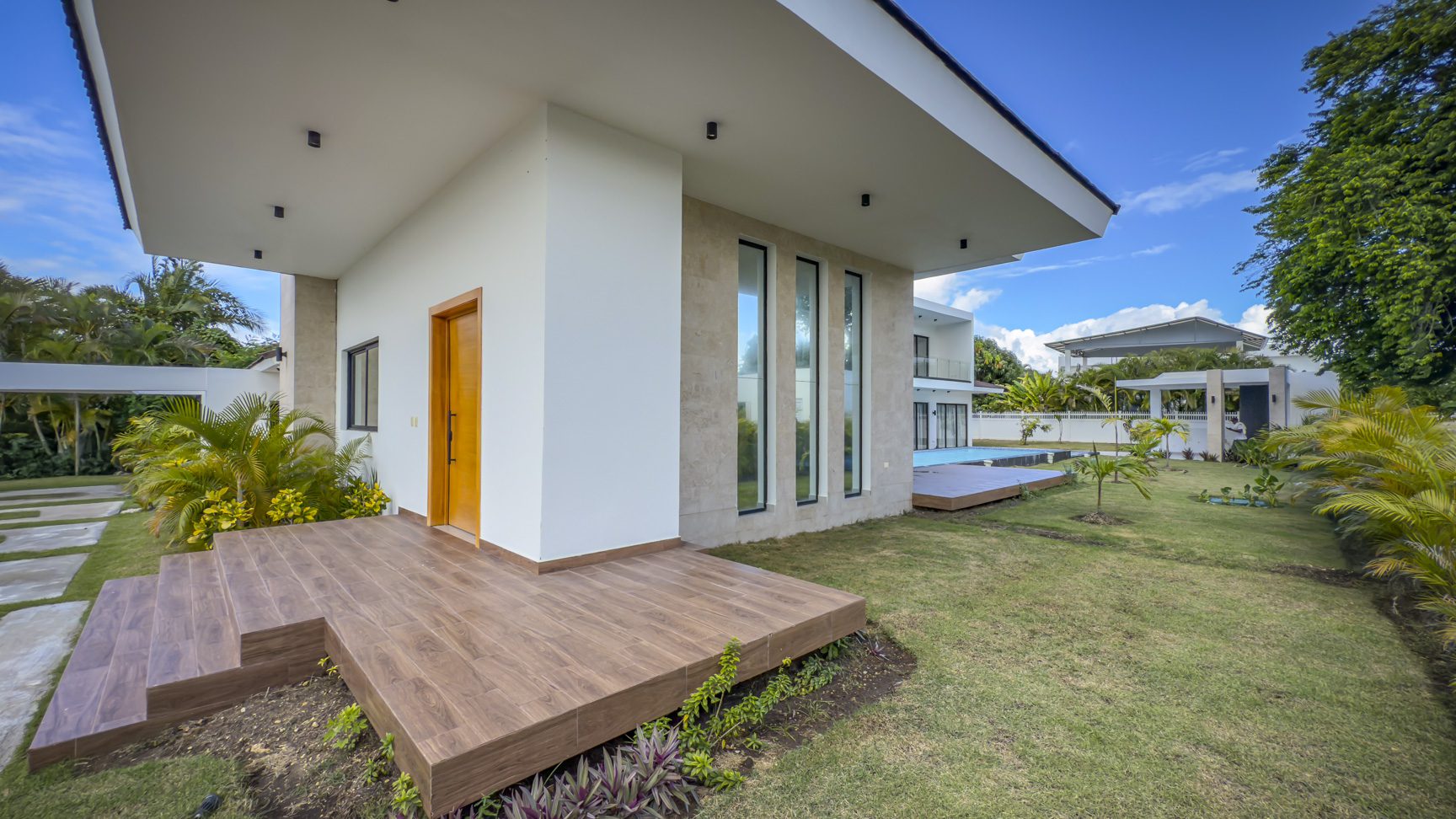 buyDRproperty Luxury villa exterior with wooden deck, modern architecture, and lush green lawn. Sosua Real Estate