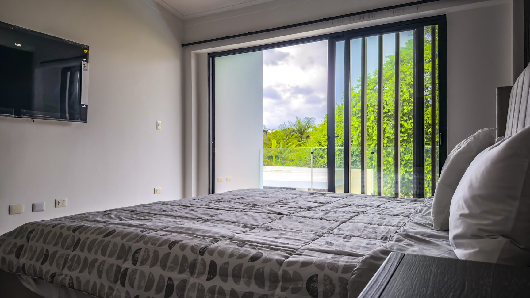 buyDRproperty Luxury villa bedroom with king bed and balcony overlooking lush greenery. Sosua Real Estate