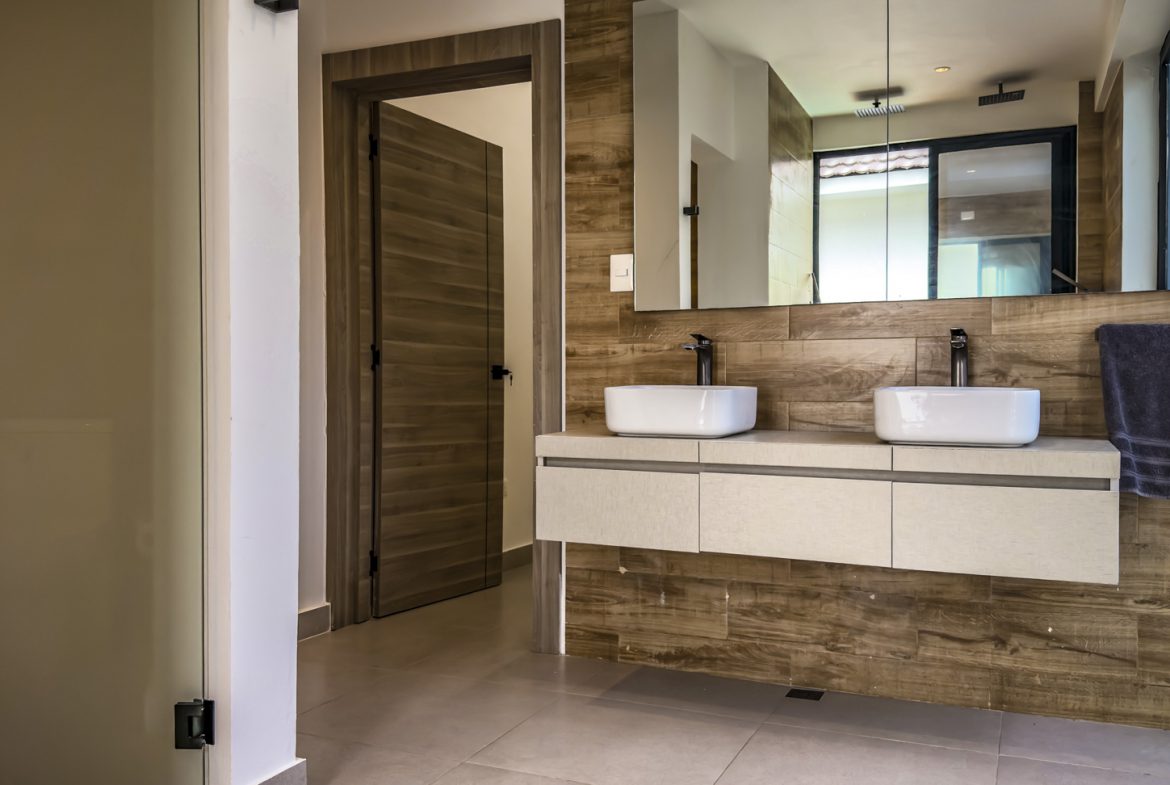 buyDRproperty Modern bathroom with double sinks and wood-look tile in a luxury Sosua villa. Sosua Real Estate
