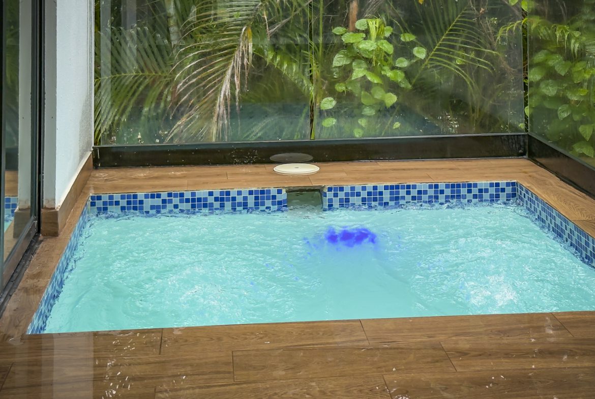 buyDRproperty Indoor plunge pool with blue lighting in a luxury Sosua villa, surrounded by lush greenery. Sosua Real Estate