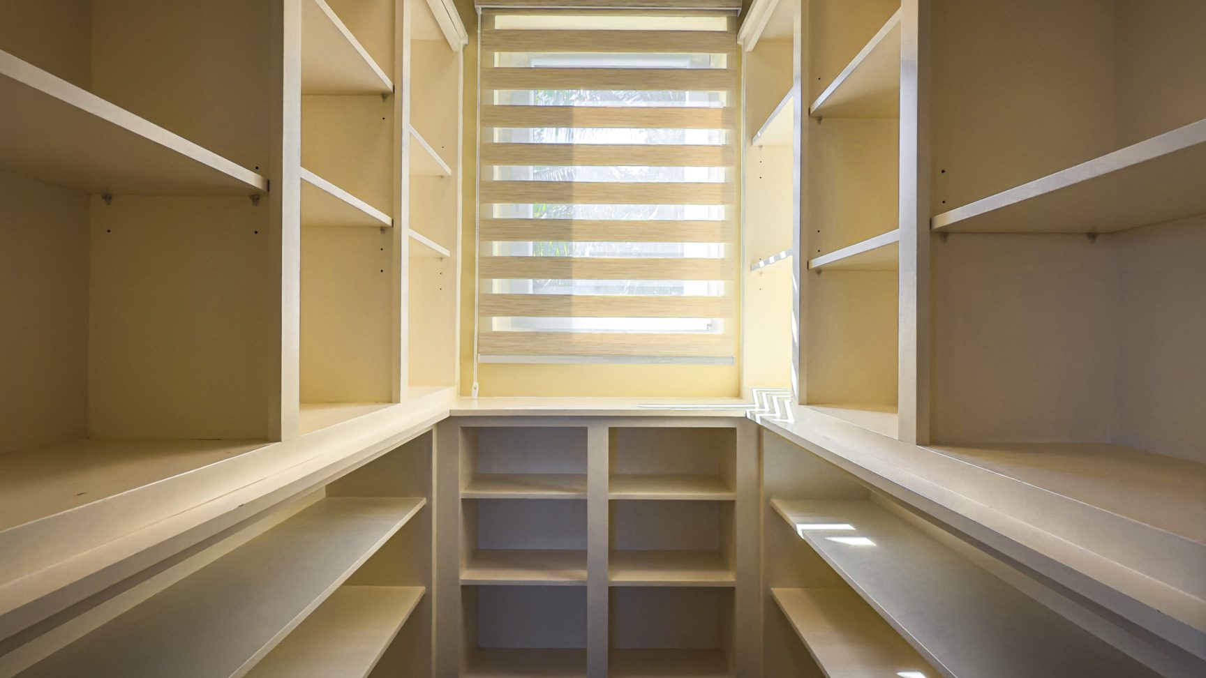 buyDRproperty Walk-in closet with built-in shelving and a window with blinds, showcasing villa interior. Sosua Real Estate