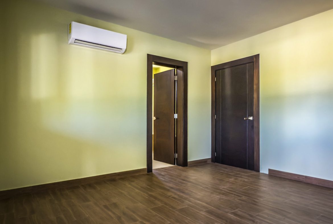 buyDRproperty Empty bedroom in a La Mulata villa for sale, featuring wood floors, two doors, and an air conditioner. Sosua Real Estate