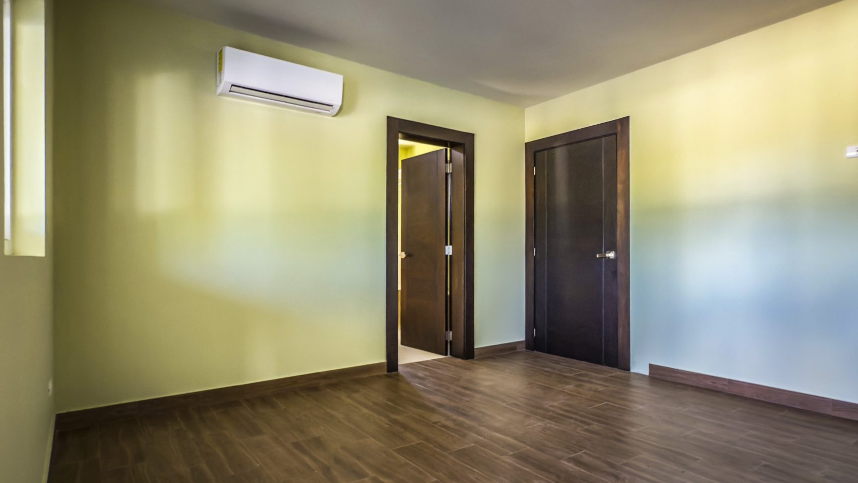 buyDRproperty Empty bedroom in a La Mulata villa for sale, featuring wood floors, two doors, and an air conditioner. Sosua Real Estate