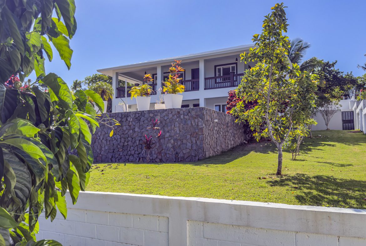 buyDRproperty La Mulata villa for sale: Three-bedroom house with stone foundation, balcony, and manicured lawn on a sunny day. Sosua Real Estate